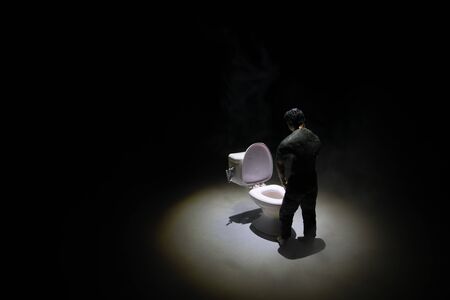 Creative concept. Miniature white toilet bowl on dark foggy background. Man peeing. Selective focusの写真素材
