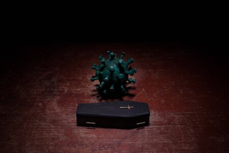 Creative artwork. Miniature wooden coffin on a table with dark background. Victims of coronavirus or...