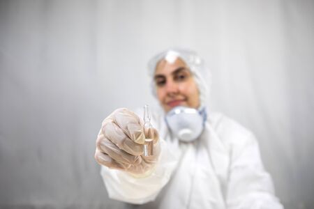 Coronavirus covid 19 infected blood vial in hand of female doctor with surgical mask and glows. Coronavirus covid 19 reseach laboratory, coronavirus covid-19 vaccine research. Selective focusの写真素材