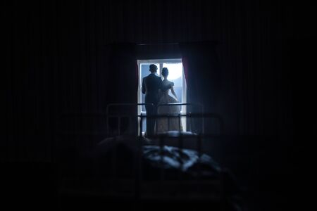 A realistic dollhouse bedroom with furniture and window at night. Romantic couple sitting on window. Man and woman making love in bedroom. Artwork table decoration . Selective focus.の写真素材
