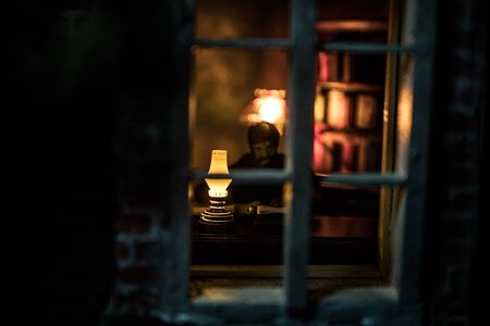 A realistic dollhouse living room with furniture and window at night. Man sitting on table in dark...