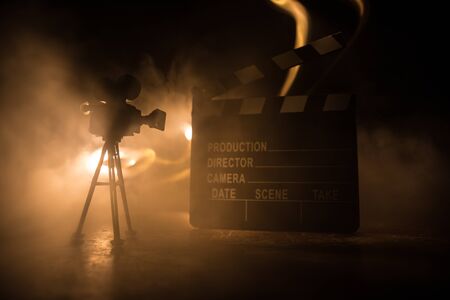 Movie concept. Miniature movie set on dark toned background with fog and empty space. Silhouette of vintage camera on tripod and clapboard. Selective focusの写真素材