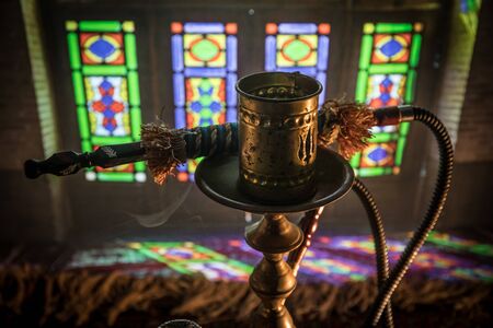 Hookah hot coals on shisha bowl making clouds of steam at Arabian interior. Oriental ornament on the...