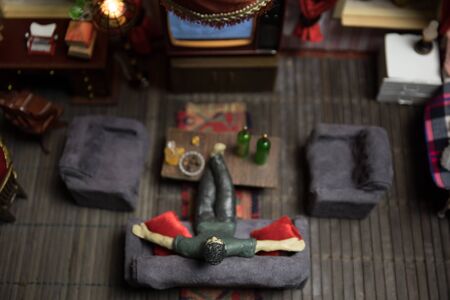 A realistic dollhouse living room with furniture and window at night. Artwork table decoration with handmade realistic dollhouse. Man wathing retro style Television in dark room. Selective focus.の写真素材