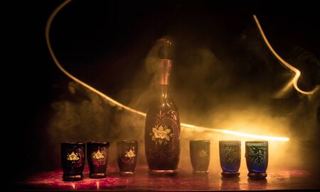 A beautiful blue carafe with vodka stands on a wooden table with glasses. Dramatic toned foggy background with light. Selective focus. Club drink concept.の写真素材