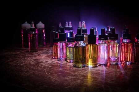 Vape concept. Smoke clouds and vape liquid bottles on dark background. Light effects. Useful as background or vape advertisement or vape background. Selective focusの写真素材