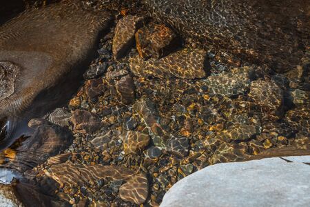 summer sunshine creates beautiful patterns on river stones under water. Nature shot