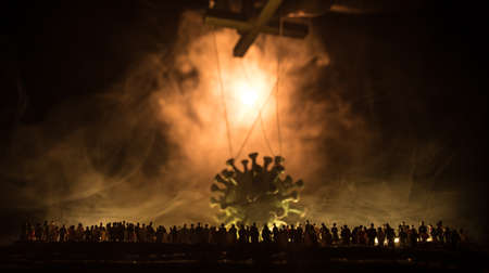 Creative concept of manipulation with coronavirus. Crowd looking on big Corona virus miniature. The hand controls the Covid19 miniature with strings on a dark foggy background. Selective focusの写真素材