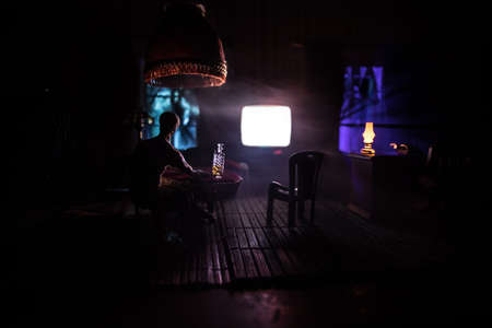 A realistic dollhouse living room with furniture and window at night. Artwork table decoration with handmade realistic dollhouse. Silhouette of a man wathing retro style Television in dark room. Selective focus.の写真素材