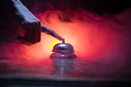 Calling service bell on wooden table with toned lights on dark background. Hotel reception bell, Hand ringing in service bell , selective focusの写真素材
