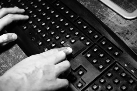 Broken keyboard with hammer on wooden table. Keyboard with no keys on dark desktop. Woman finger on...