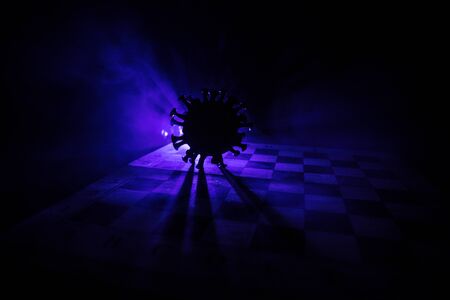 Chess board game concept strategy of business in Covid global pandemic. Big Corona virus miniature model on chessboard with fog and backlight. Creative artwork decoration. Selective focusの写真素材