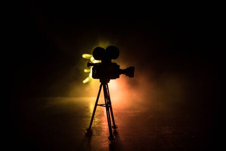 Movie concept. Miniature movie set on dark toned background with fog and empty space. Silhouette of vintage camera on tripod. Selective focusの写真素材