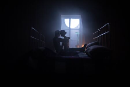 A realistic dollhouse bedroom with furniture and window at night. Romantic couple sitting on window. Man and woman making love in bedroom. Artwork table decoration . Selective focus.の写真素材