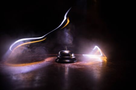 Calling service bell on wooden table with toned lights on dark background. Hotel reception bell, service bell on the table, selective focusの写真素材