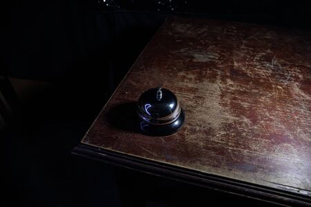 Calling service bell on wooden table with toned lights on dark background. Hotel reception bell, service bell on the table, selective focusの写真素材