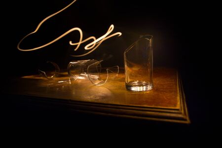 Drink, broken glass concept. Broken glasses on wooden table at dark toned background with fog....