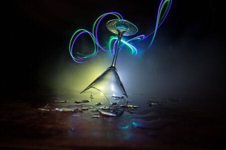 Drink, broken glass concept. Broken glasses on wooden table at dark toned background with fog....