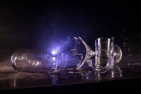 Drink, broken glass concept. Broken glasses on wooden table at dark toned background with fog. Selective focusの写真素材