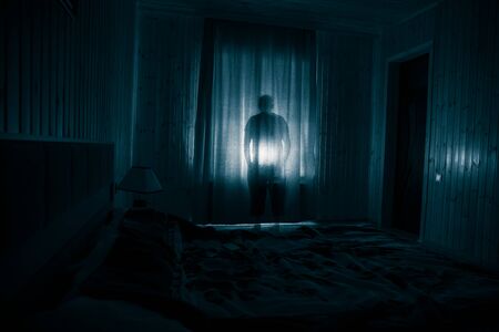 Horror silhouette in window with curtain inside bedroom at night. Horror scene. Halloween concept....
