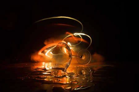 Drink, broken glass concept. Broken glasses on wooden table at dark toned background with fog. Selective focusの写真素材