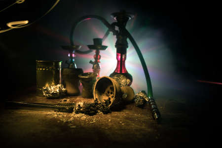 Shisha concept. Preparing shisha on table. Used shisha bowl on wooden table. Dark atmosphere with light. Selective focus.の写真素材
