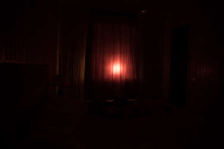 Light in window with curtain inside bedroom at night. Horror scene. Halloween concept. Blurred silhouette of ghostの写真素材
