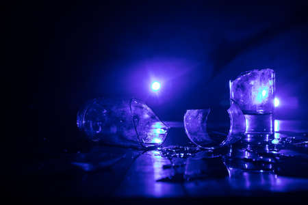 Drink, broken glass concept. Broken glasses on wooden table at dark toned background with fog. Selective focusの写真素材