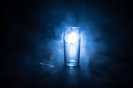 Drink, broken glass concept. Broken glasses on wooden table at dark toned background with fog. Selective focusの写真素材