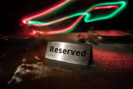 Reserved sign on the table. A tag of reservation placed on the wood table. Metal tag with reservation on dark. Reserved table in a restaurant. Creative concept with colorful lights. Selective focusの写真素材