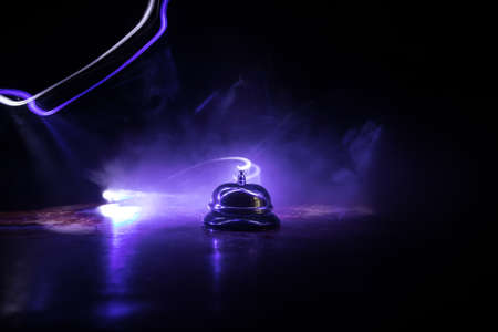 Calling service bell on wooden table with toned lights on dark background. Hotel reception bell,...