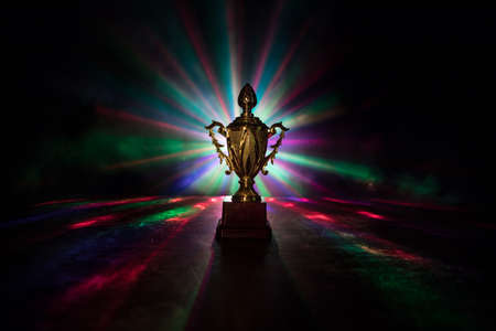 Golden trophy cup on table dark background with copy space. Creative artwork decoration with toned foggy backlight. Selective focusの写真素材