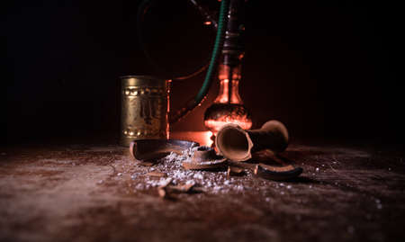 Shisha concept. Broken shisha bowl on wooden table. Dark atmosphere with light. Selective focus.