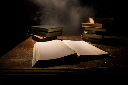 A stack of old books. Vintage book on wooden table. Magic lightning around a glowing book in the room of darkness. Selective focusの写真素材