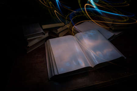 A stack of old books. Vintage book on wooden table. Magic lightning around a glowing book in the room of darkness. Selective focusの写真素材