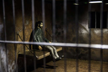 Man in prison man behind bars concept. Old dirty grunge prison miniature. Dark prison interior creative decoration. Selective focusの写真素材