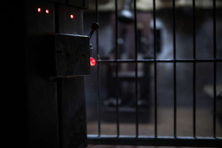 Execution concept. Death penalty electric chair miniature in selective focus inside old prison. Old prison bars cell lock. Creative artwork decoration. Electric chair scale model in the darkの写真素材
