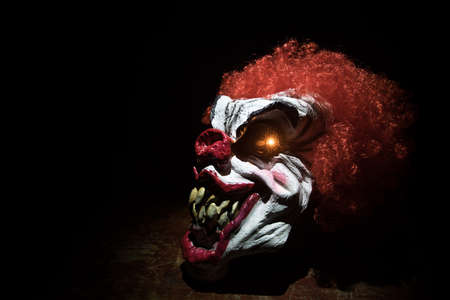 Spooky Clown head on wooden table. Evil clown smiling on dark foggy background. Halloween concept....
