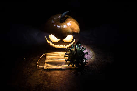 Halloween during Corona virus global pandemic concept. Glowing pumpkins and Covid novel on dark with...