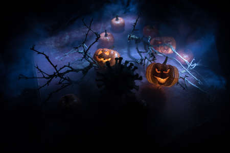 Halloween during Corona virus global pandemic concept. Glowing pumpkins and Covid novel on dark with thematic spooky decorations. Halloween pumpkin on foggy backlight. Selective focusの写真素材