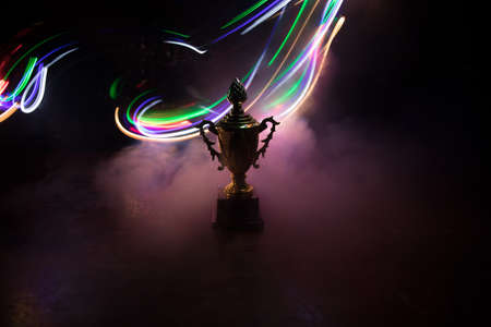 Golden trophy cup on table dark background with copy space. Creative artwork decoration with toned foggy backlight. Selective focusの写真素材