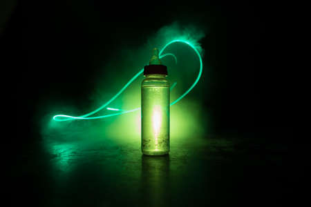 Close up of baby bottle at wooden table on dark toned foggy background with light. Creative artwork decorated photo. Selective focus.の写真素材