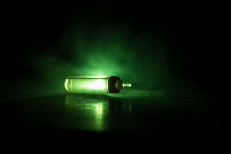 Close up of baby bottle at wooden table on dark toned foggy background with light. Creative artwork...