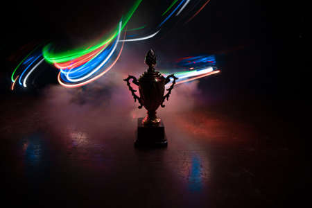 Golden trophy cup on table dark background with copy space. Creative artwork decoration with toned foggy backlight. Selective focusの写真素材