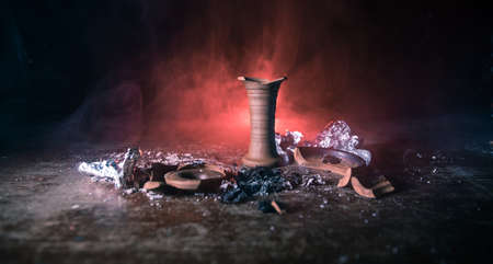 Shisha concept. Broken shisha bowl on wooden table. Dark atmosphere with light. Selective focus.
