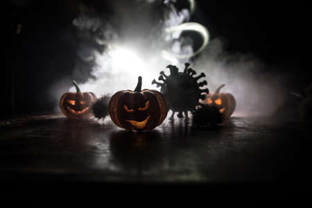Halloween during Corona virus global pandemic concept. Glowing pumpkins and Covid novel on dark with...