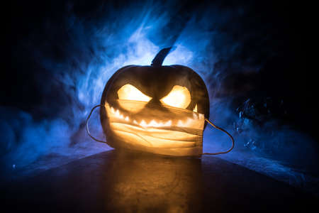 Halloween during Corona virus global pandemic concept. Glowing pumpkins and Covid novel on dark with thematic spooky decorations. Halloween pumpkin on foggy backlight. Selective focusの写真素材