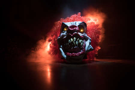 Spooky Clown head on wooden table. Evil clown smiling on dark foggy background. Halloween concept. Selective focusの写真素材