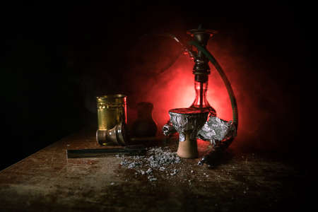 Shisha concept. Preparing shisha on table. Used shisha bowl on wooden table. Dark atmosphere with light. Selective focus.の写真素材