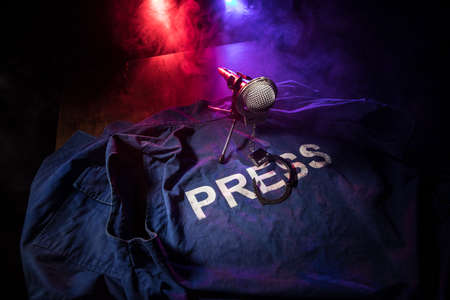 Freedom of the press and journalism concept. Blue journalist (press) vest in dark with backlight and fog. Microphone and handcuffs. Selective focusの写真素材